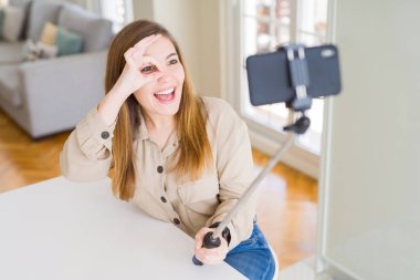 Mutlu yüzü ile selfie çubuğu kullanarak fotoğraf çeken güzel genç kadın parmaklarından bakarak eliyle ok işareti yapıyor gülümseyerek