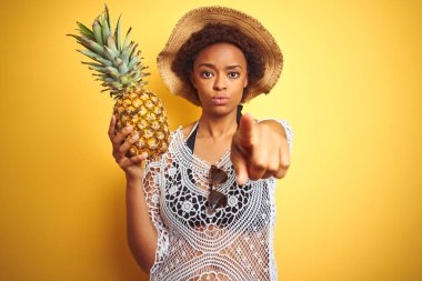 Afro saç tutan genç Afrikalı Amerikalı kadın sarı izole arka plan üzerinde kamera ve size, el işareti, ön pozitif ve emin jest parmak ile işaret üzerine Pineaple