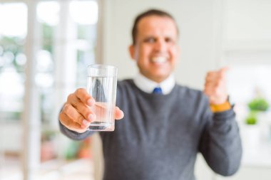 Orta yaş adam ev işaret ve mutlu yüz gülümseyen yanında başparmak ile gösteren su içme bardağı