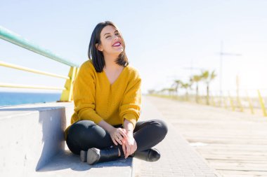 Güzel genç kadın bir mesire neşeli zevk güneş ışığı güneşli günde rahatlatıcı gülümseyen deniz kenarında oturup...