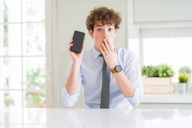 Genç iş adamı ofis kapağı ağız, hata için utanç ile şok, korku ifadesi, sessizlik, gizli kavram korkuyor ile telefon ekranı gösteren