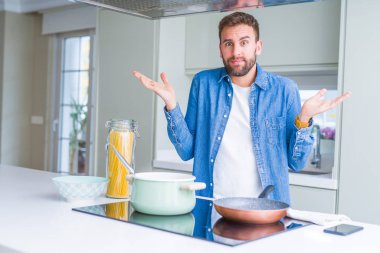Yakışıklı adam mutfakta İtalyan spagetti makarna pişirme clueless ve kollar ve elleri ile karıştı ifade kaldırdı. Şüphe kavramı.