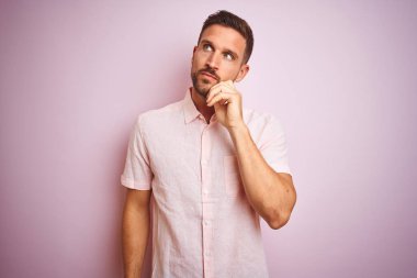 Genç yakışıklı adam soru, dalgın ifade hakkında düşünme çene üzerinde el ile pembe izole arka plan üzerinde zarif yazlık gömlek giyiyor. Düşünceli bir yüzle gülümsüyor. Şüphe kavramı.