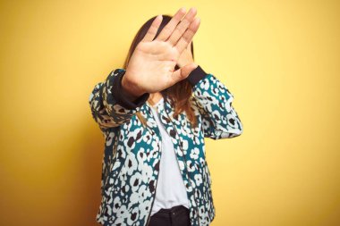 Genç güzel kadın el ile gözler kapsayan sarı izole arka plan üzerinde rahat ceket giyiyor ve üzücü ve korku ifadesi ile stop jest yapıyor. Utanç verici ve negatif kavram.