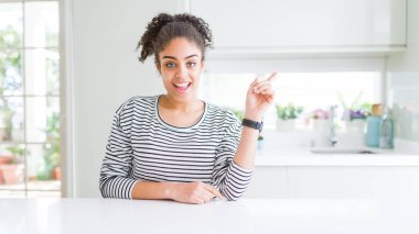 Afro saçlı güzel afro-amerikan kadın yüzünde büyük bir gülümseme ile rahat çizgili kazak giyen, kameraya bakarak yan el parmağı ile işaret.