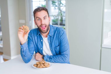 Yakışıklı adam çikolata Çerezler bir sürpriz yüz, korkuyor ve heyecanlı korku ifadesi ile şok korkmuş yeme