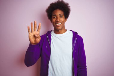 İzole pembe arka plan üzerinde ayakta mor sweatshirt giyen genç Afrikalı Amerikalı adam gösteren ve parmak sayısı dört ile işaret kadar güven ve mutlu gülümseyen.