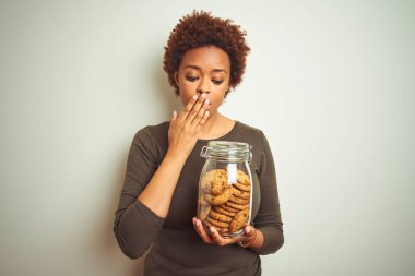 Afrikalı Amerikalı kadın, yanlışlıkla utanç ile şok, korku ifade, sessiz, gizli kavramı korkmuş el ile izole arka plan kapak ağzına çikolata cips kurabiye tutan kavanoz