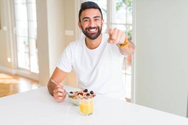 Yakışıklı İspanyol adam sabah evde kamera parmak ile işaret ve size, el işareti, pozitif ve ön emin jest sağlıklı kahvaltı yeme