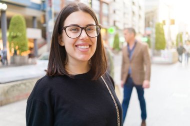 Şehir sokaklarında yürürken heyecanlı gülümseyen güzel genç esmer kadın, şehirde açık havada mutlu ve güven ifade ayakta