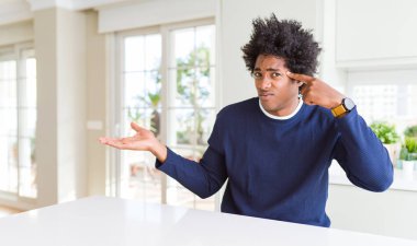 Evde oturan rahat kazak giyen genç Afrikalı Amerikalı adam karıştı ve açık palmiye gösteren kopya alanı ve alnına parmak işaret ile rahatsız. Bunu düşün..