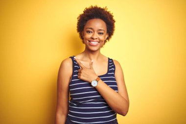 Mutlu ve doğal ifade ile yan yukarı el ve parmak ile işaret yüzünde bir gülümseme ile izole sarı arka plan üzerinde yaz t-shirt giyen beauitul Afrikalı Amerikalı kadın