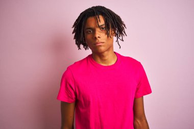 Yüzünde ciddi bir ifade ile izole pembe arka plan üzerinde duran t-shirt giyen dreadlocks ile Afro Amerikan adam. Kameraya basit ve doğal bir bakış.