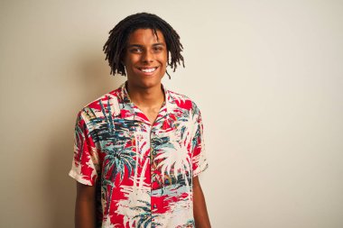 Yüz üzerinde mutlu ve serin bir gülümseme ile izole beyaz arka plan üzerine yaz gömlek giyen tatil dreadlocks ile Afro adam. Şanslı kişi.