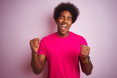 Afro saç ile genç Amerikan adam izole pembe arka plan üzerinde ayakta tişört giyen çok mutlu ve heyecanlı silah ile kazanan jest yaparak, gülümseyen ve başarı için çığlık kaldırdı. Kutlama konsepti.