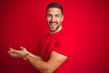 Kırmızı izole arka plan üzerinde rahat t-shirt giyen genç yakışıklı adam el açık avuç içi gösteren kopya alanı ile bir kenara işaret, reklam gülümseyen heyecan mutlu sunmak