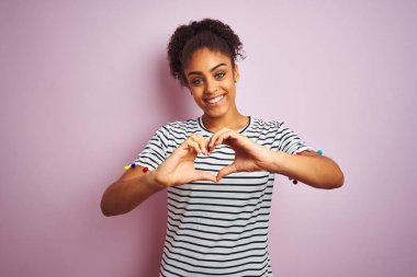 Lacivert çizgili t-shirt giyen Afro-amerikan kadın izole pembe arka plan üzerinde duran sevgi kalp sembolü ve elleriyle şekil gösteren gülümseyerek. Romantik kavram.