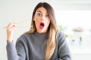 Evde Asya Chopsticks tutan genç güzel kadın sürpriz bir yüz ile şok korkmuş ve korku ifadesi ile heyecanlı korkuyor
