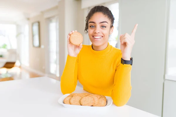 Young african american girl eating healthy whole grain biscuits very happy pointing with hand and finger to the side