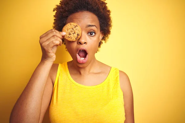 Afrikanische Amerikanerin Mit Schokoladenkeks Über Gelbem Hintergrund Erschrocken Mit Einem — Stockfoto