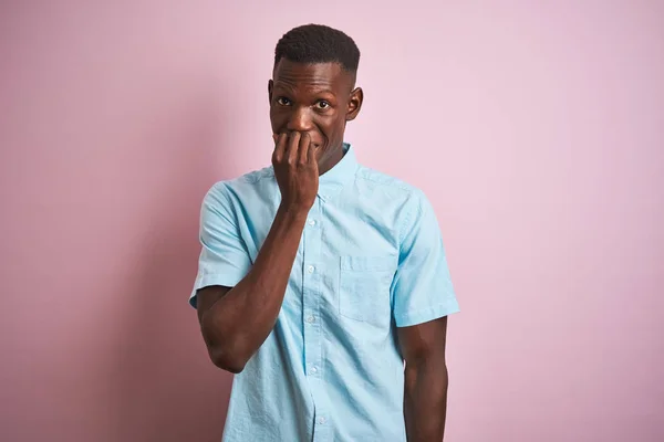 孤立したピンクの背景の上に立つ青いカジュアルなシャツを着たアフリカ系アメリカ人男性は 口を噛む爪に手を当て ストレスと緊張を見ています 不安の問題 — ストック写真