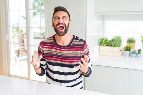 英俊的西班牙男子穿着条纹毛衣在家里疯狂和疯狂的喊叫和大喊 咄咄逼人的表情和手臂提高 挫折概念 — 图库照片