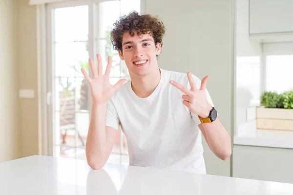 自宅で白いTシャツを着た若いハンサムな男は 自信を持って幸せに微笑みながら 指番号8を示し 指を上げる — ストック写真