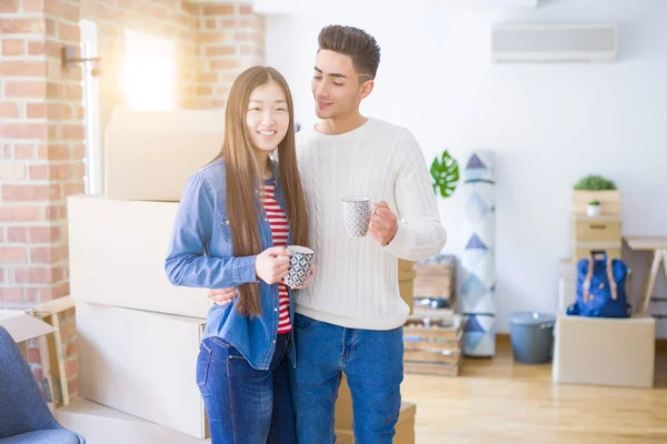 Молода азіатська пара п'є чашку кави в новому будинку, посміхаючись — стокове фото