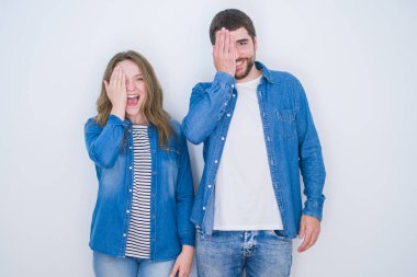 Beyaz izole arka plan üzerinde birlikte ayakta genç güzel çift el ile bir göz kaplayan, yüz ve sürpriz duygu kendine güvenen gülümseme.