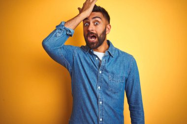 Denim gömlek giyen genç hintli adam izole sarı arka plan üzerinde duran hata için kafasına el ile şaşırttı, hata hatırlıyorum. Unuttum, kötü bellek kavramı.