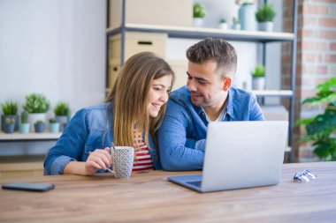 Genç çift bir kahve içme rahatlatıcı ve karton kutular etrafında bilgisayar laptop kullanarak, çok mutlu yeni bir eve hareket