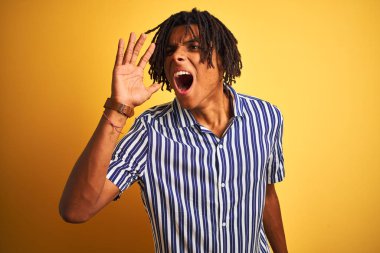 Kıvırcık sarı arka plan üzerinde rahat çizgili t-shirt giyen dreadlocks ile Afro adam bağırma ve ağzına el ile yan gürültülü çığlık. İletişim konsepti.