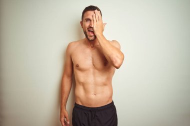 El ile bir göz kapsayan izole arka plan üzerinde genç yakışıklı gömleksiz adam, yüz ve sürpriz duygu kendine güvenen gülümseme.