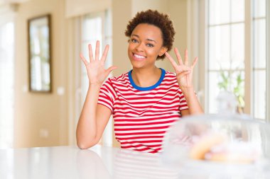 Genç güzel Afrikalı-Amerikalı kadın evde gösterilen ve parmak dokuz ile gülümseyen ise kendinden emin ve mutlu yukarı dönük.