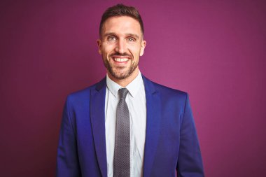 Yüz üzerinde mutlu ve serin bir gülümseme ile mor izole arka plan üzerinde genç yakışıklı iş adamı. Şanslı kişi.