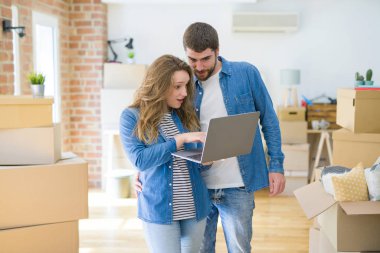 Yeni bir daireye taşımak için mutlu karton kutular etrafında bir odada bilgisayar laptop ayakta kullanarak genç çift