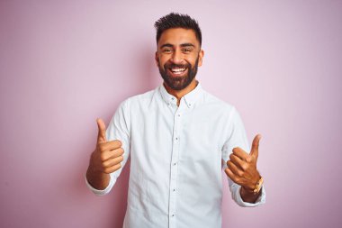 Genç Hintli işadamı izole pembe arka plan başarı işareti üzerinde ayakta zarif gömlek giymiş el ile olumlu jest yapıyor, gülümseyen ve mutlu yukarı başparmak. Neşeli ifade ve kazanan jest.