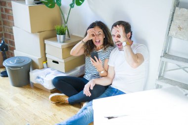 Mutlu yüzlü akıllı telefon kullanarak yeni bir eve taşınan orta yaş yaşlı çift parmaklarından bakarak el ile ok işareti yapıyor gülümseyerek