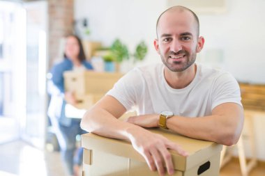 Genç çift yeni daireye hareket, yakışıklı adam karton kutular hareketli ve mutlu gülümseyerek