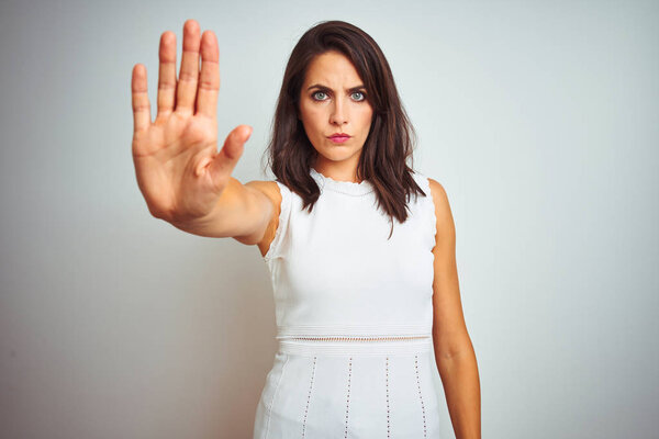 Young beautiful woman wearing dress standing over white isolated background doing stop sing with palm of the hand. Warning expression with negative and serious gesture on the face.