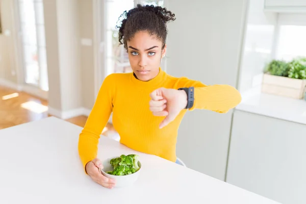 年轻的非洲美国女孩吃热绿色花椰菜与愤怒的脸 负面的迹象显示不喜欢与拇指向下 拒绝概念 — 图库照片