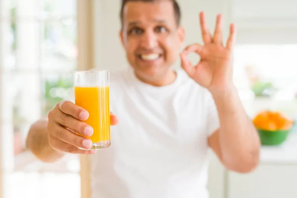 中年男子喝一杯橙汁在家里做好标志用手指 优秀的符号 — 图库照片