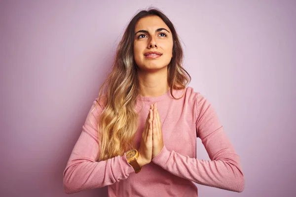 Young beautiful woman wearing a sweater over pink isolated background begging and praying with hands together with hope expression on face very emotional and worried. Asking for forgiveness. Religion concept.