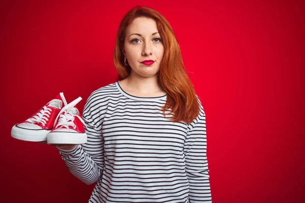 Jovem Bela Ruiva Mulher Segurando Tênis Sobre Vermelho Isolado Fundo — Fotografia de Stock