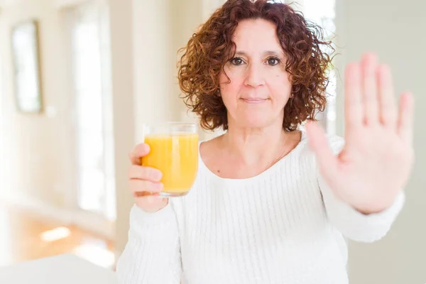 高级妇女用张开的手打一杯新鲜的橙汁 用严肃而自信的表情做停止标志 辩护手势 — 图库照片