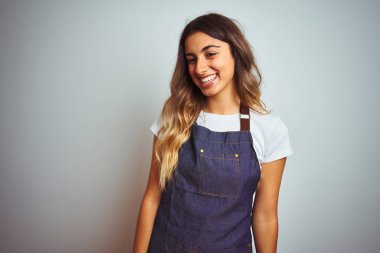 Genç güzel kadın gri izole arka plan üzerinde yüz gülümseme ile yan bakmak, doğal ifade üzerinde apron giyiyor. Güven gülüyor.