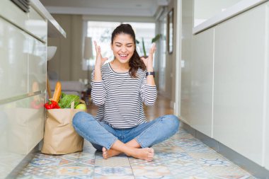 Mutfak zemininde oturan genç kadın taze bakkaliye dolu bir poşetle delice ve çılgın bir şekilde başarı için kolları kaldırıp, gözleri kapalı çığlık atarak heyecanla bağırıyor. Kazanan kavramı