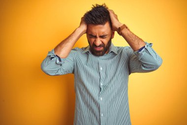 Genç Hint adam üzerinde ayakta yeşil çizgili gömlek giymiş izole sarı arka plan baş ağrısı umutsuz ve vurguladı çünkü ağrı ve migren. Eller baş.