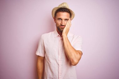Pembe izole arka plan üzerinde şapka ve Yaz gömlek giyen yakışıklı adam yorgun görünümlü ve çapraz silah ile depresyon sorunları ile sıkılmış düşünme.
