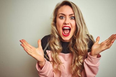 Beyaz izole arka plan üzerinde ayakta sweatshirt giyen genç çekici kadın deli kutluyor ve başarı için hayran silah kaldırdı ve açık gözleri heyecanlı çığlık. Kazanan kavramı